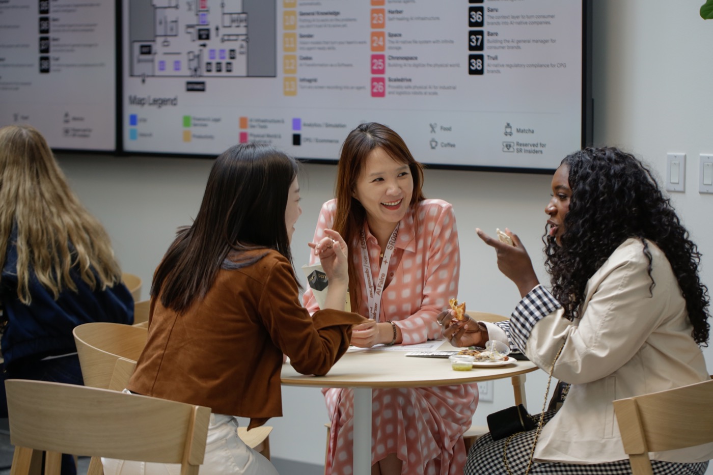 Three people talking over food at a table, with an event map on the screen behind them